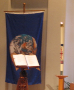 Earth Day banner, Bible, and Paschal candle combine to illustrate the themes of the day.