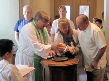 April and David Olsen hold their son as Pastor Jeff baptizes him.